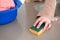 Close up of woman`s hands cleaning kitchen counter top with a scouring pad. Nearby they have bucket with rags