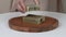 A close-up of woman`s hands putting bars of natural lavender soap on a round wooden tray. On the top she puts two bars