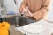 Close up of woman`s hands scrubbing a dirty glass with a yellow scouring pad under a kitchen faucet