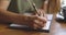 Close up of woman's hands writing down on a white blank notebook with cup on wooden table