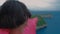 Close up woman with short trendy hair standing on edge of cliff above blue ocean and pointing finger on distant island