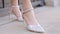 Close-up of woman in stylish white shoes. Action. Luxurious white shoes on beautiful legs of woman. Stylish design of