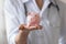 Close up woman wearing white coat, doctor holding piggy bank