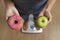 Close up woman on weight scale holding in her hand apple fruit and donut as choice of healthy versus unhealthy food