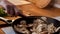 Close-up of woman with wooden spatula interferes with chopped champignon mushrooms in pan. Slow motion video