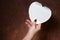 Close up of womanâ€™s hand holding white heart-shaped notepad, brown background