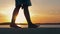 Close-Up Of Women Feet Are On The Beach In The Flicker Rays Of The Sunset