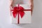 Close-up women hands sending white gift box with red ribbon on white background