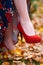 Close up of women`s feet shod in red high heels shoes, autumn season, yellow fallen leaves as background