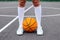 Close up wonan`s feet in white sneakers and whote long socks, with a ball on a basketball court.