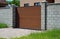 A close-up of a wood slat automatic sliding gate, entrance driveway sliding gate, gray brick fence with pillars, and paver