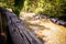 Close up of a wooden handrail in a forest near a river in which a group of persons make trakking in summer