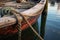 close-up of wooden rowboat tied with rope to dock post