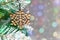 Close-up of a wooden snowflake hanging from a fir branch against a bokeh background. Simple christmas composition with free space