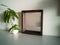 Close up of wooden stained mirror against the wall with plants.