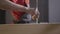 Close up of a workman in coverall applying glue with a brush inside the hole of a wooden beam on blurred background