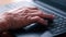 Close-up of the wrinkled hand of an elderly man working on a laptop.