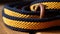 a close up of a yellow and blue rope with a leather ring on a wooden surface with a wood handle and a black and white stripe