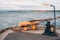 Close-up of yellow metallic mooring column or bollard on the edge of stone quay blue water background. Marine Bollard