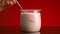 Close-up of yogurt in glass cup on red background. Stock footage. Hand with spoon takes yogurt from glass on isolated