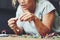 Close up of young adult woman busy in jewelry cheap wooden beads making of braelets and necklace. Alternative home work for modern