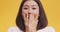 Close up of young amazed asian lady opening mouth and touching face in astonishment, yellow studio background