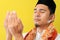 Close-up of a young Asian Muslim man praying raising his hands wearing Muslim dress, low angle and close-up