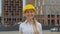 Close up of the young attractive Caucasian cheerful woman builder in the hard yellow helmet smiling to the camera