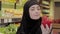 Close-up of young beautiful Muslim woman smelling red bell pepper. Portrait of positive cute girl in hijab choosing