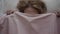 Close-up of young blond caucasian woman looking out from under pink blanket and hiding again. Portrait of positive cute