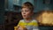 Close up of young boy holding piece of orange fruit in hands, eating it in slow motion. Kid enjoying fresh orange on