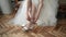 Close-up of young bride's hands in white wedding dress as she dons pretty white wedding shoes