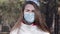 Close-up of young brunette woman in protective mask and gloves coughing in sunny spring park. Portrait of sick Caucasian