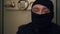 Close-up of young caucasian thief in black clothes and balaclava looking at camera. The guy stealing things from safe