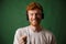 Close-up of young curly readhead hipster holding cord of headphones, looking at camera