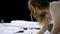 Close up of young fair-haired woman standing bending over working table in tailoring studio and drawing future dresses