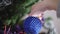 Close-up of young female Caucasian hand hanging ball on decorated Christmas tree. Unrecognizable woman decorating house