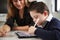 Close up of young female teacher sitting at desk with a Down syndrome schoolboy using a tablet computer in a primary school classr