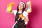 Close up of young fun housewife in orange gloves, brown apron, white t shirt, hair band. Housekeeper woman shoots from spray