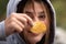 Close up of a young girl holding a potato chip in front of her face, wearing a hooded sweatshirt