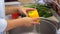 Close-up of a young girl washing yellow bell peppers at home in the kitchen. 4K