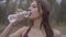 Close-up of young gorgeous sportswoman drinking water in park and leaving. Portrait of confident brunette girl training