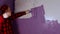 Close up of young man dancing and painting wall in purple colour with roller. Happy male applying paint on wall. Concept