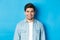 Close-up of young man feeling awkward, smile and cringe from uncomfortable situation, standing over blue background