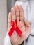 Close up of a young man holds in hand red ribbon and showing hand gesture to stop. World AIDS day concept vertical shot