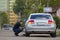 Close-up of young man pumping tire of shiny expensive silver car on the road on blurred green trees, moving taxi and buildings sum