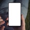 Close up of a young man sitting long holding smartphone with the white screen. Person is on-line from a smartphone