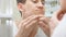 Close up of young man standing close to a mirror in the bathroom and squeezing a pimple on his face