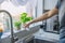 Close up Young Man watering home gardening on the kitchen windowsill. Pots of herbs with basil and watercress sprouts. Home