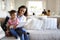 Close up of young mother sitting on sofa in the living room with her toddler on her knee reading him a book, father and sister sit